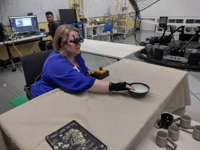 A research team member who is blind uses acoustic touch to locate and reach for an item on the table.   Image Credit: Photo taken by Lil Deverell (co-author) at the Motion Platform and Mixed Reality Lab in Techlab at the University of Technology Sydney (UTS), Australia, CC-BY 4.0