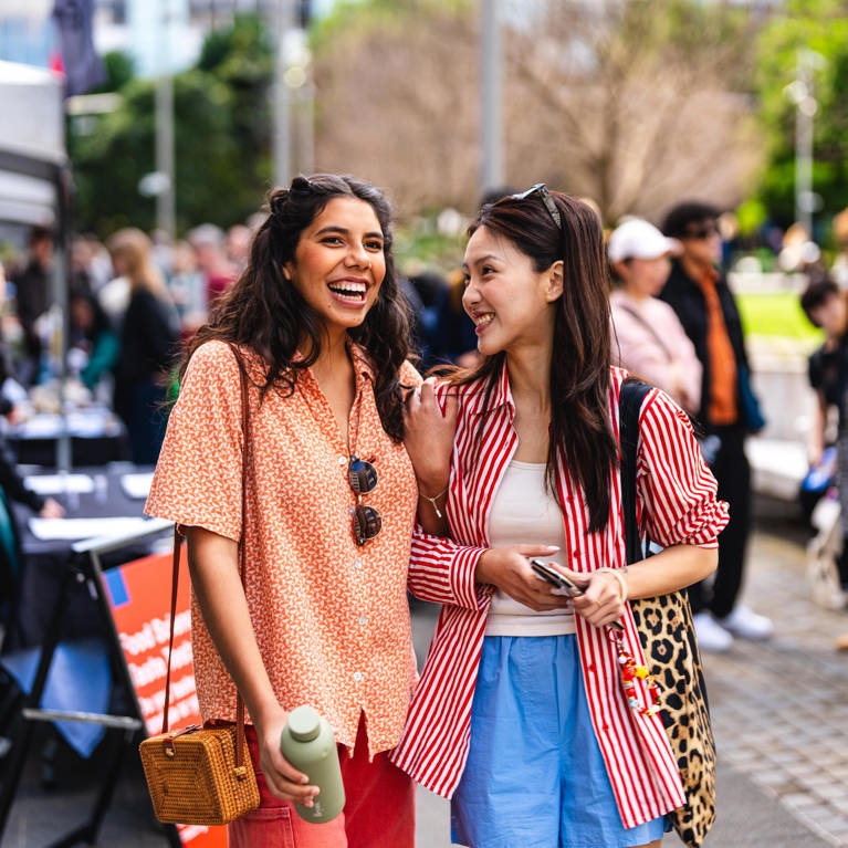 Two UTS prospective students stand side by side at university Open Day event, enjoying the atmosphere and engaging with the surrounding crowd.