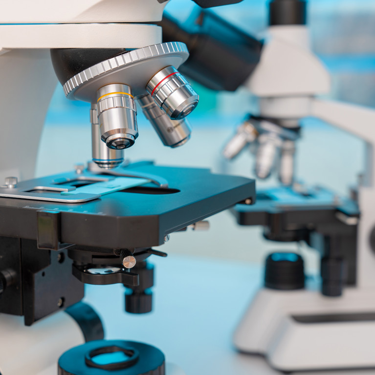 Close-up of two white microscopes in a lab. The focus is on their lenses and eyepieces, conveying a sense of scientific inquiry and precision.