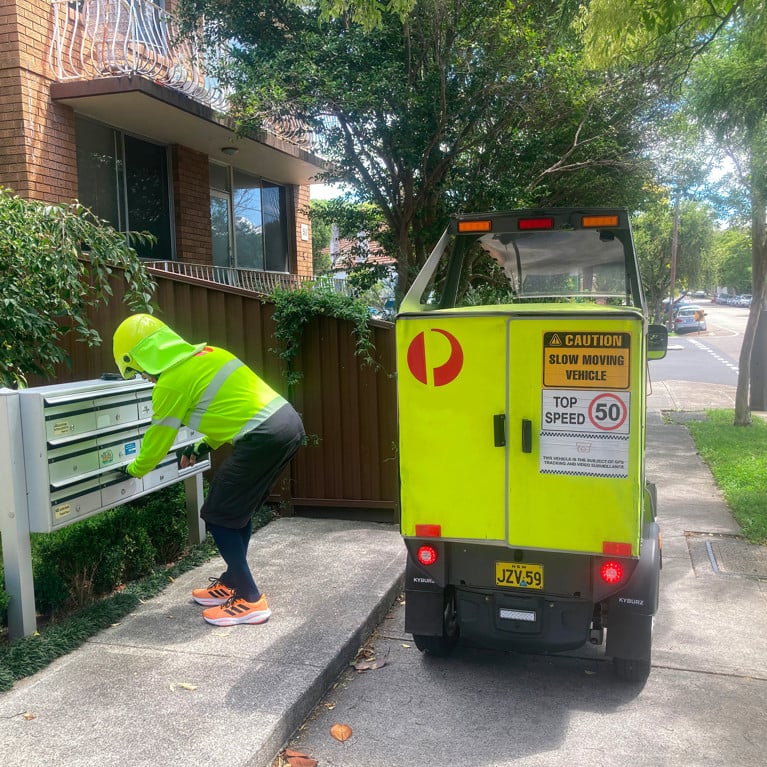 Sydney, NSW Australia - February 18 2023: An Australia Post postman wearing hi-vis delivering the mail to a letter box with his hi-vis van. Picture: Rose Makin/Adobe Stock