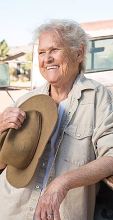 woman leans on truck laughing with hat in hand