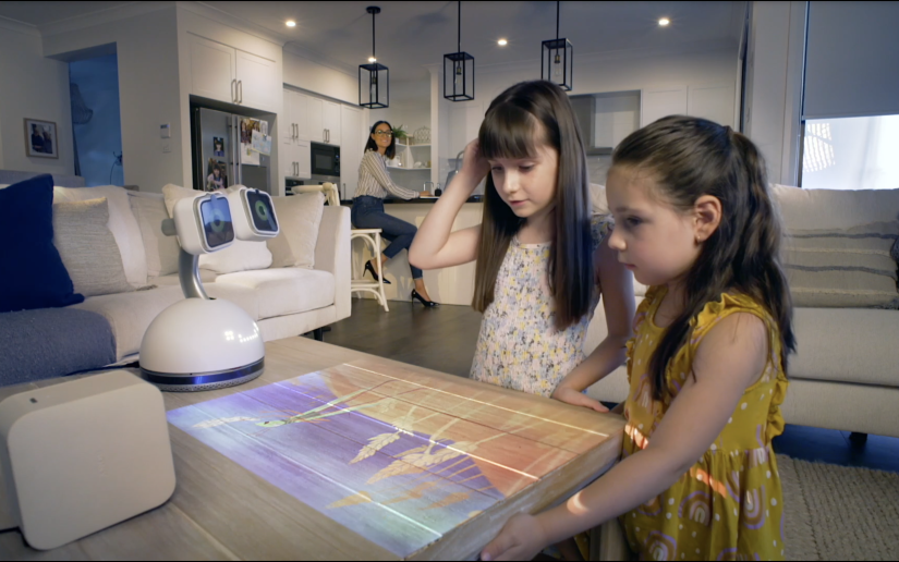Haru the Social robot in storytelling mode projects an image onto a table while two young girls look on.