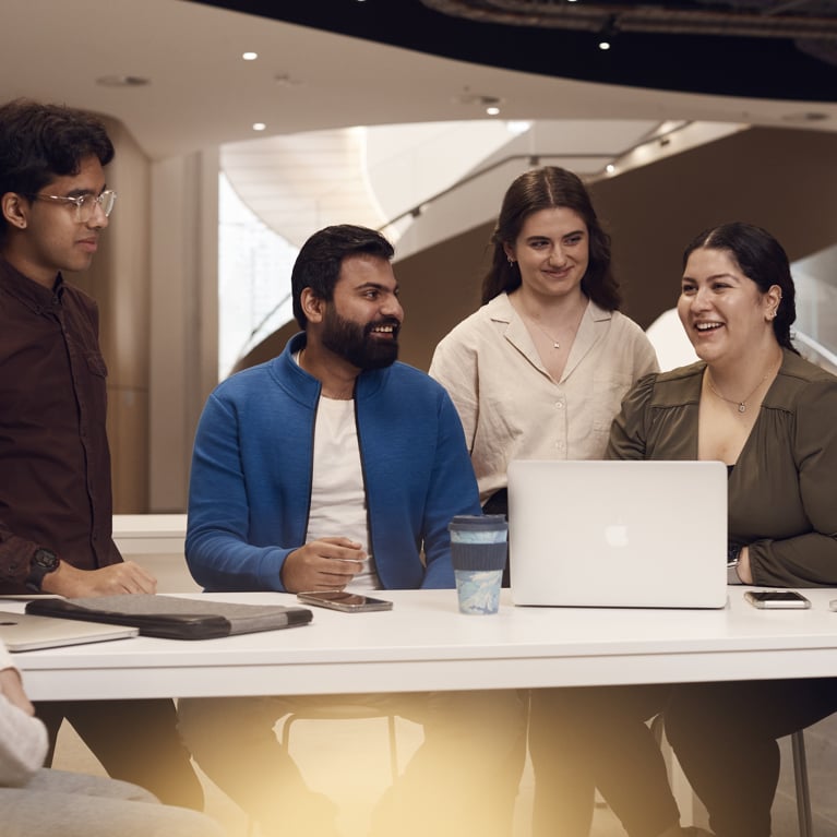A diverse group of students gathered around a table, collaborating with a laptop inside a UTS building.