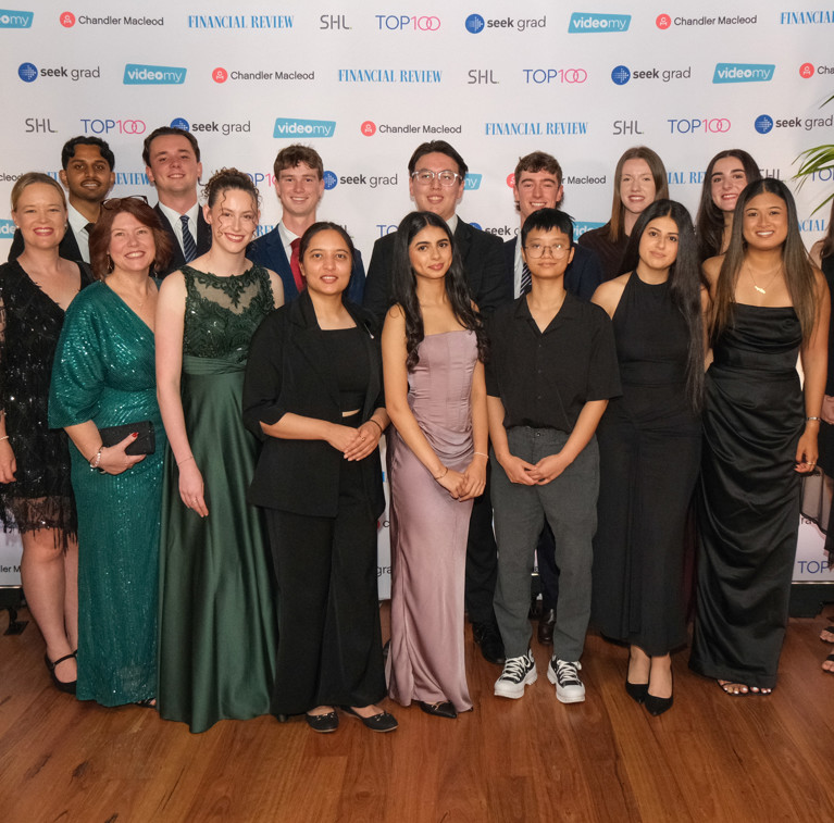 UTS staff and nominated students standing in front of a sponsors media wall at the SEEK Grad Top100 Future Leaders Awards night