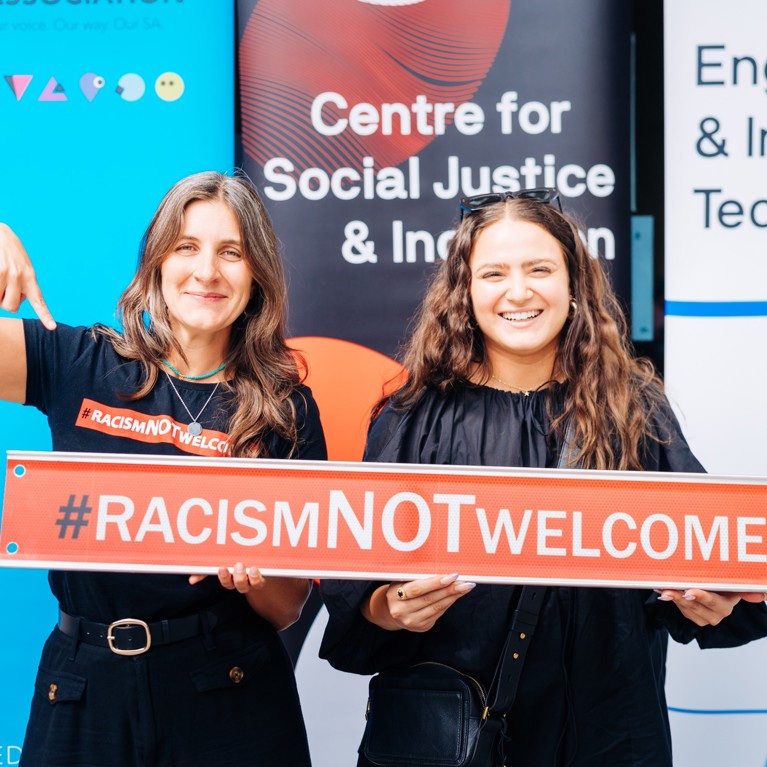 Two University of Technology Sydney staff members holding a 'Racism NOT Welcome' sign