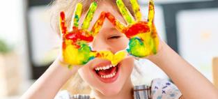 Child laughing, showing hands covered with paint