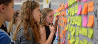 school students look at sticky notes on a wall. Adobe Stock