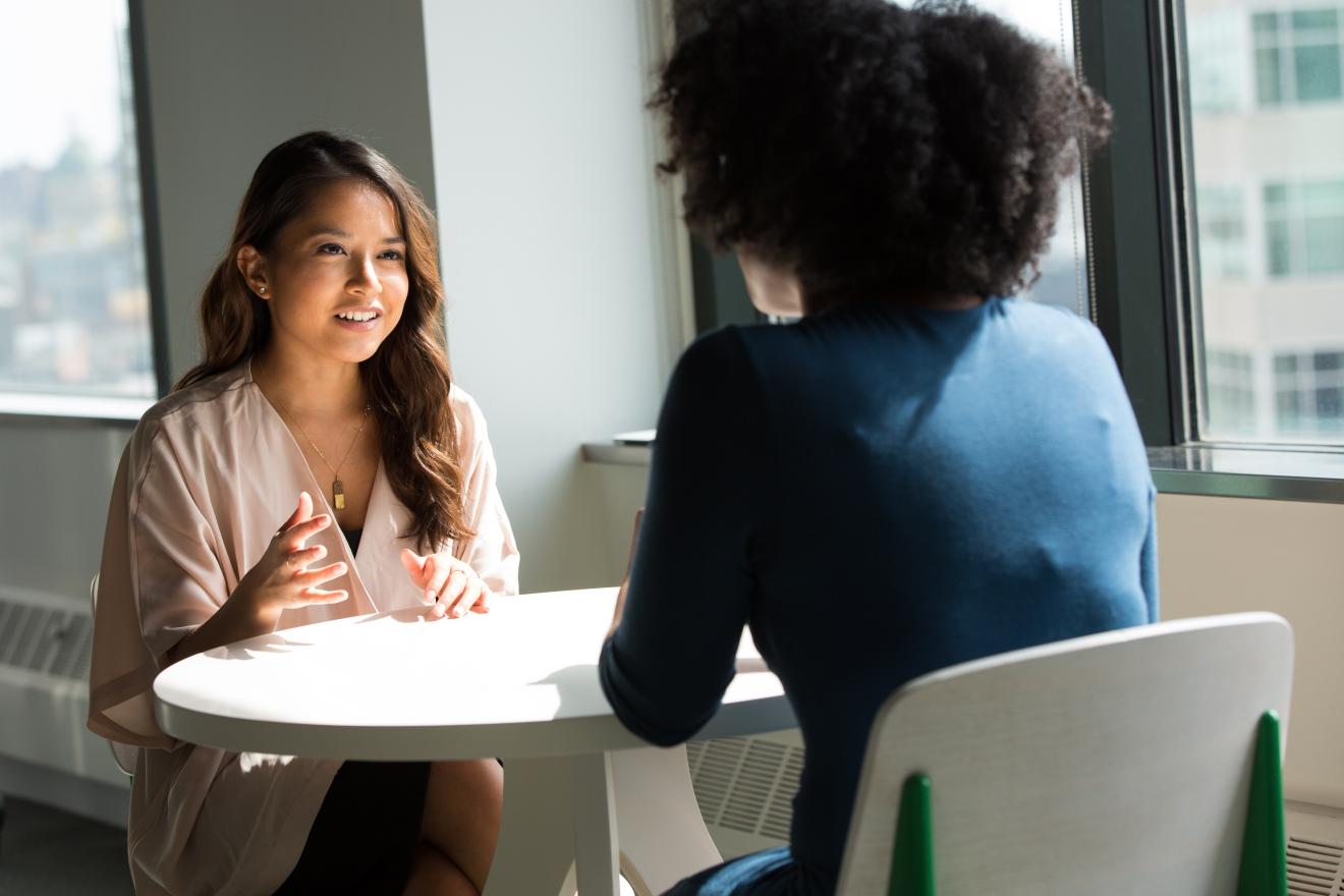 Two students sitting and talking at a round white table. 