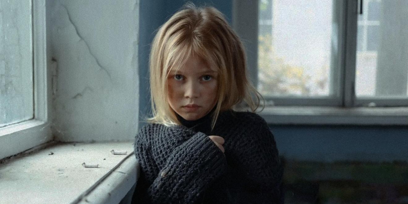 A young girl in a tattered blue jumper looking to camera. 