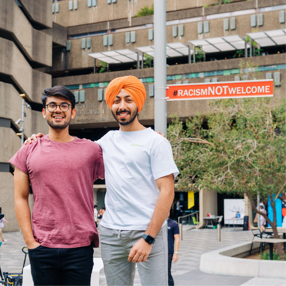 Two male students posing with the #RACISMNOTWELCOME sign on the UTS Alumni Green.