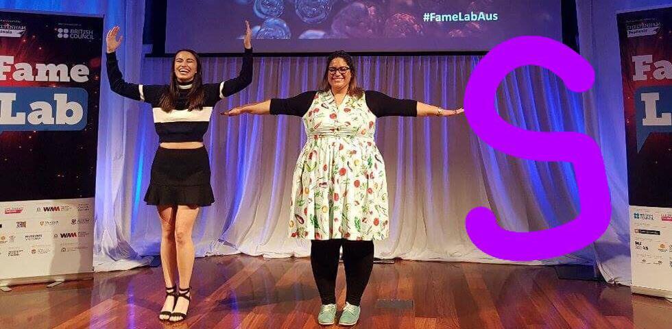 Two female scientists on stage with arms outstretched.