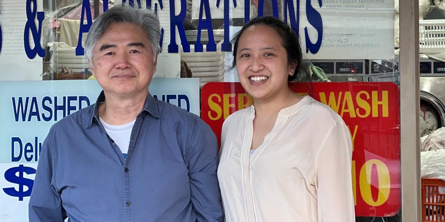 Elderly man with a young female relative standing in front of a laundry shop smiling and looking at the camera