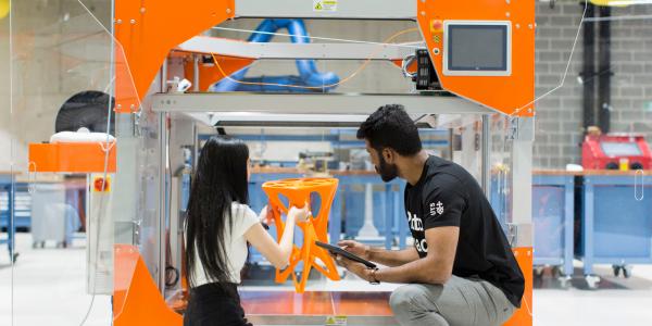Two people take the finished product out of a large 3D Printer