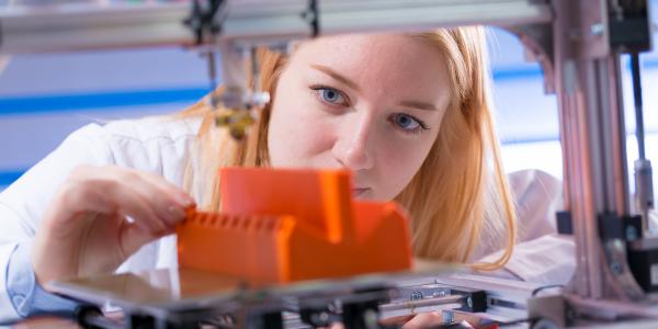 A female student inspects her bright orange additive 3D printed object