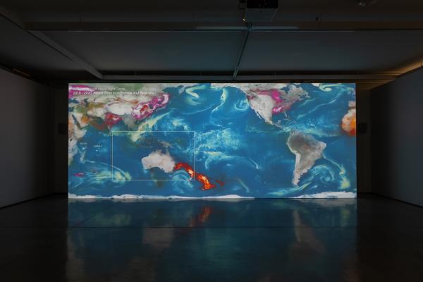 A large projection screen in a darkened room showing a world map. The east coast of Australia is on fire.