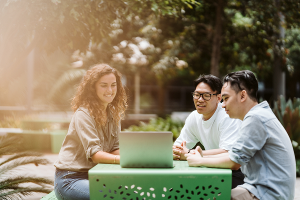 Students sit at green table and look at laptop