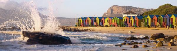 A view looking across a beach with small colourful houses lined up on the edge of the high tide mark