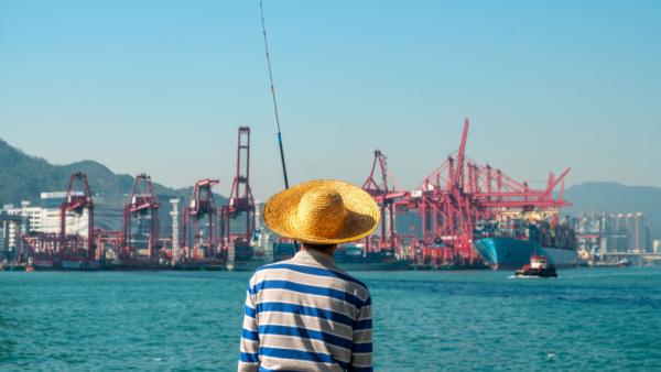 800x450 Fisher man with fishing rod from behind near container ship and freight harbour