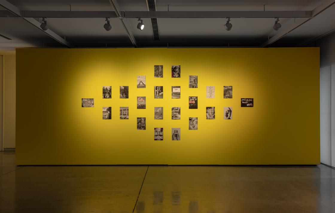 A series of black and white collages displayed on a yellow wall 