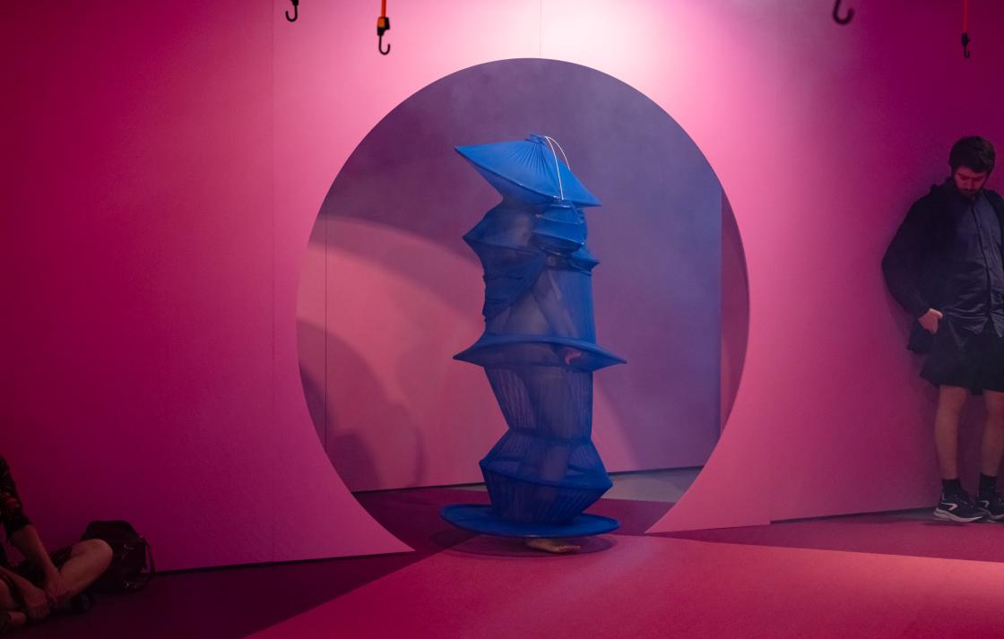 A person in a blue costume emerges from a round doorway painted pink