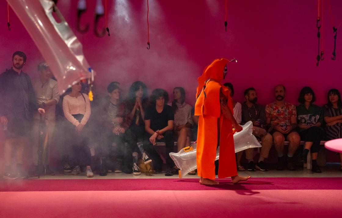 A person in an orange costume walks on a runway