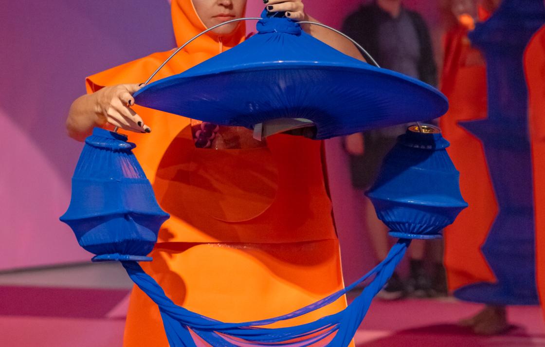 A person in an orange costume hangs a blue headpiece on an octopus strap