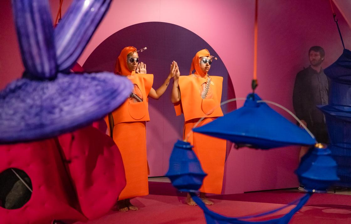 Two people in orange costumes hold hands in a rounded doorway