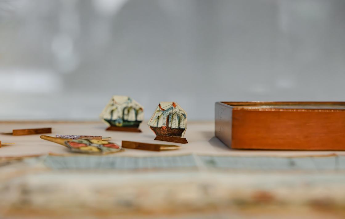 A close up view of children's game pieces; two paper ships and a spinning wheel