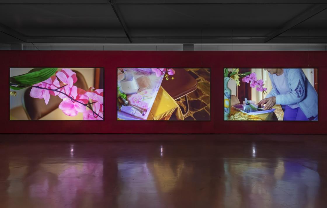 A three channel video work in a gallery with red walls 