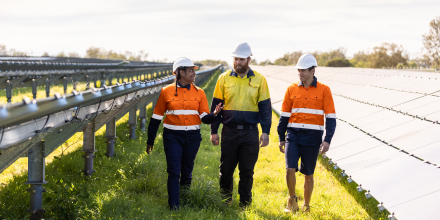 Three renewable energy workers walking through a solar panel field.