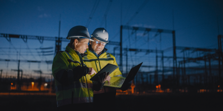 Two energy workers in PPE discussing something within an energy grid area.