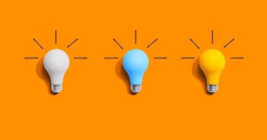 Idea and creativity concept with white, blue and yellow light bulbs laying flat on an orange background.