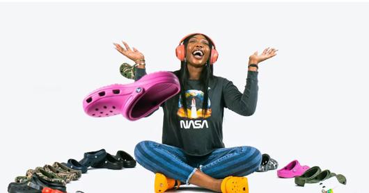 A woman sits smiling surrounded by crocs