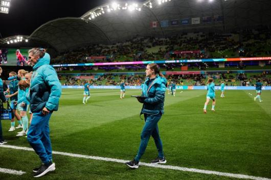 Georgia Brown on the field with the Matildas in the background 