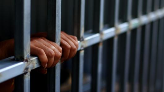 Hands on bars in jail. Adobe Stock