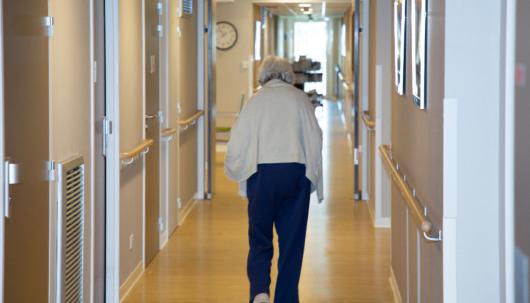 Elderly woman walks down hallway in aged care home. Adobe Stock