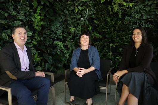 Three people sitting in front of green plant background.