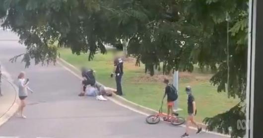 A screenshot from YouTube shows two security guards standing over a person who is on the ground in a park.