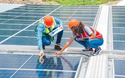 Two workers installing solar panels on a roof