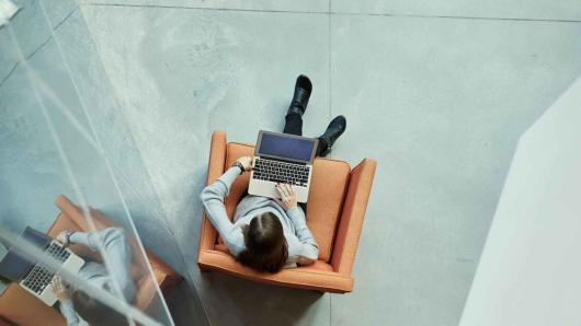 Overhead shot of a woman working on a laptop while sitting in a brown armchair