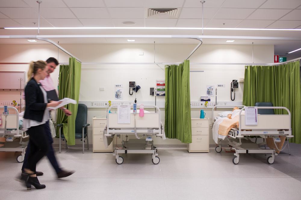2 people holding charts walk past hospital beds