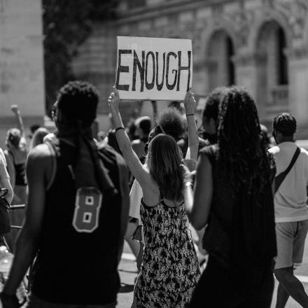 Black and white image of a woman holding a sign that says 'ENOUGH'