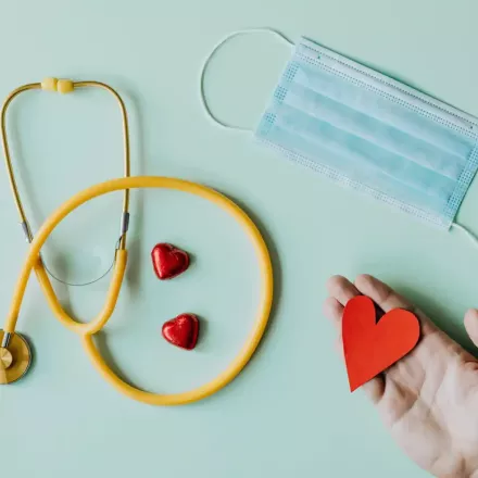 hand holding paper heart with mask and stethescope on table