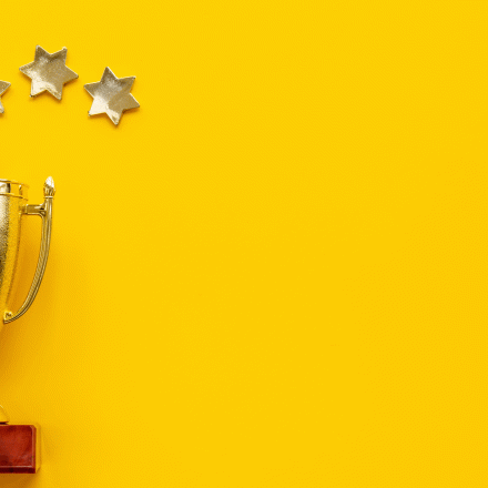 Shiny gold trophy with 5 small shiny gold stars above it on a bright yellow background