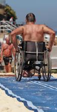 A man in a wheelchair is seated at a beach, looking content as he enjoys the fresh air and natural surroundings.