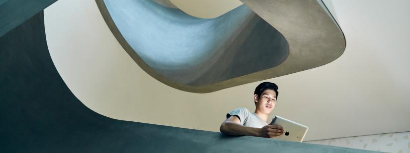 male student standing in a stairwell using an iPad