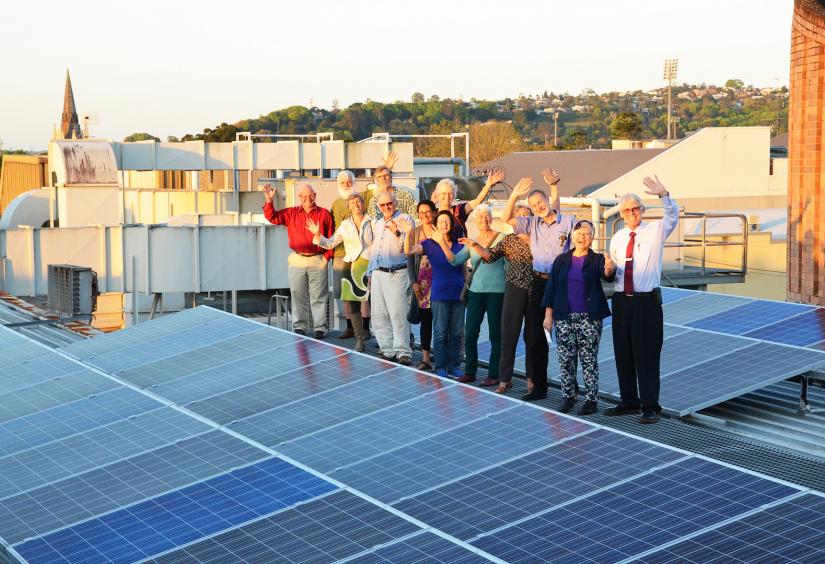 People waving behind solar panels - Photo courtesy of Lismore Workers Club