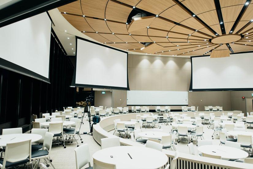 Modern conference room with screens on the walls and round tables across the floor.