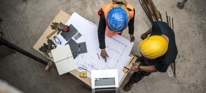 Two colleagues discuss blueprints at a worksite