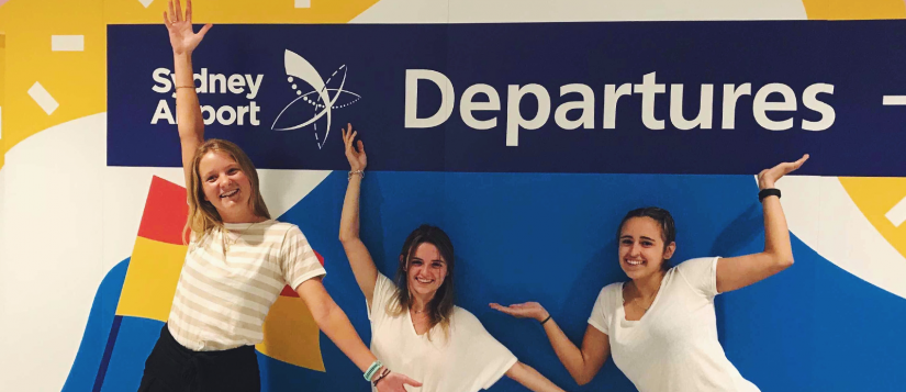 A group of students standing in front of a Departures sign at the airport